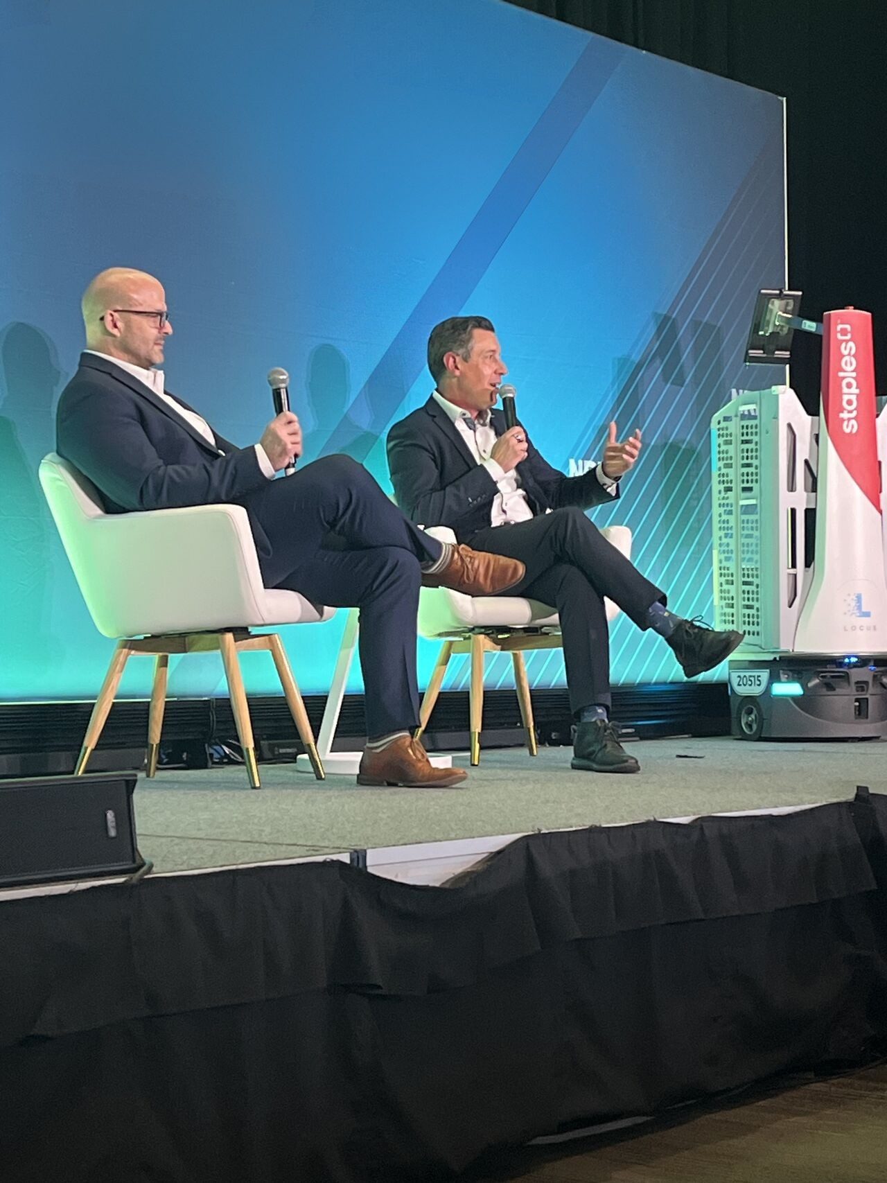 Two men on stage at a conference with a Locus Origin robot