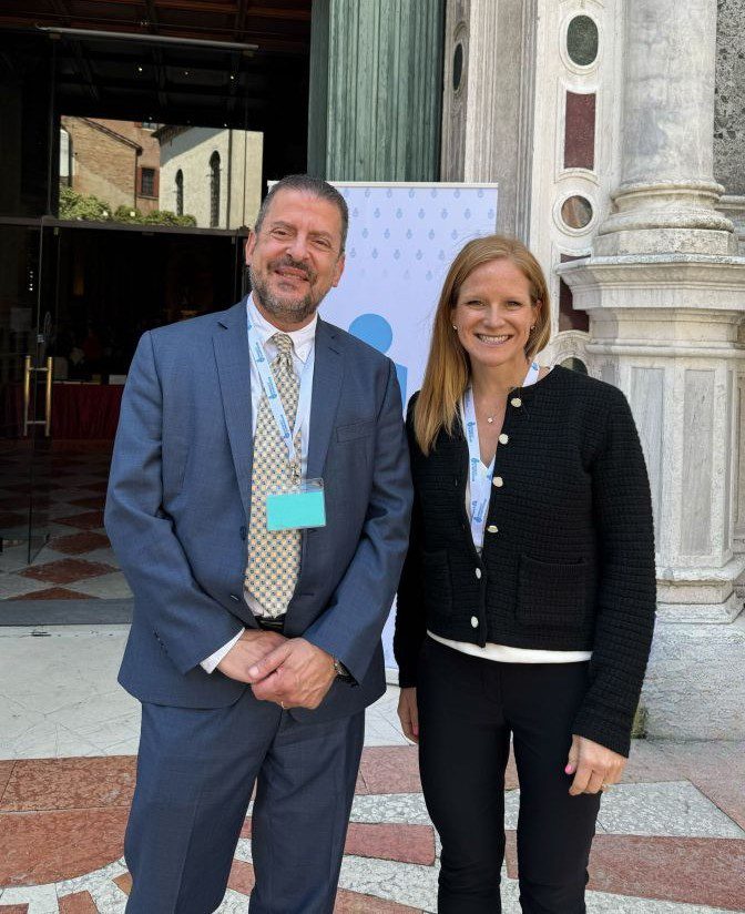 Two conference attendees wearing lanyards posing outside a historic marble building at an event