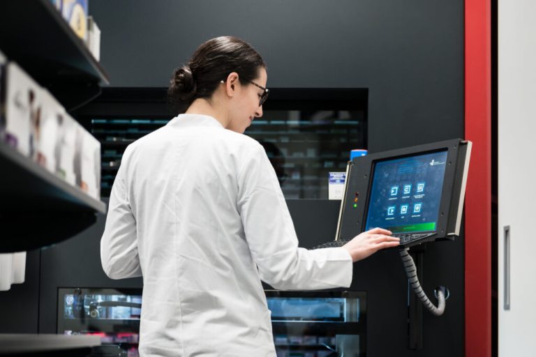 Pharmacist in a white coat using a touchscreen terminal on an automated pharmacy dispensing system