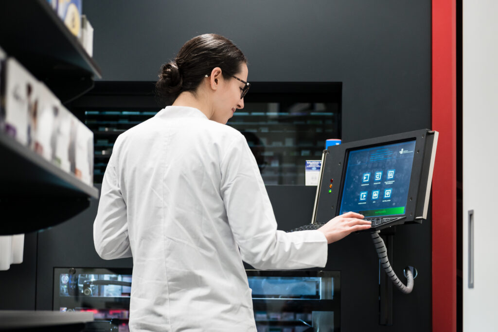 Pharmacist in a white coat using a touchscreen terminal on an automated pharmacy dispensing system