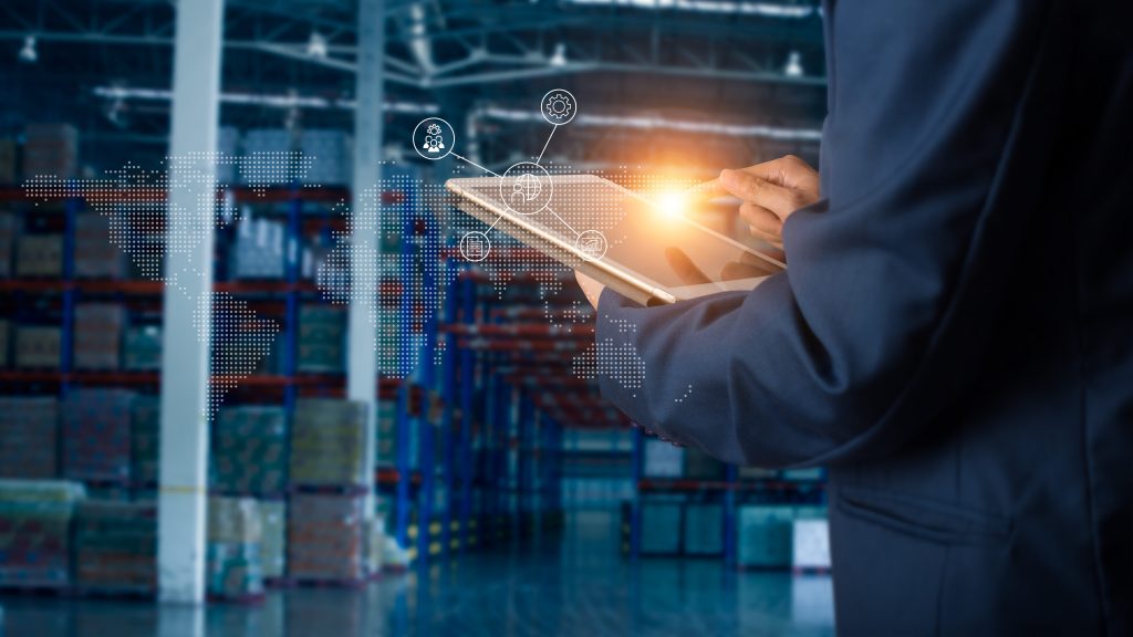 Manager using a tablet with digital network icons in a stocked warehouse aisle