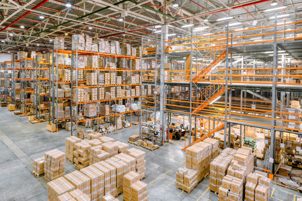 Large warehouse with orange pallet racking, a multi-level mezzanine with stairs and stacked cartons