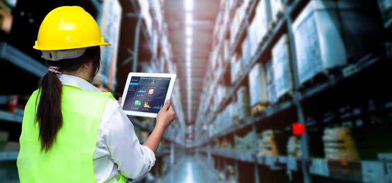 Worker in a hard hat viewing a warehouse management dashboard on a tablet in a storage aisle