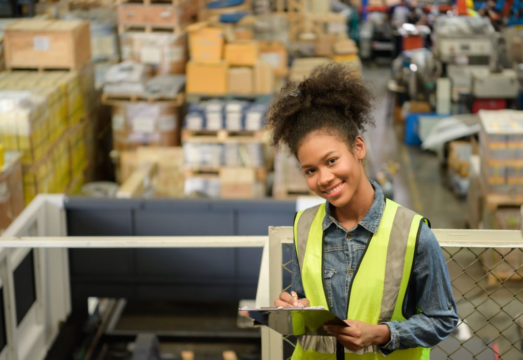 Smiling worker in a safety vest holding a clipboard on an elevated warehouse mezzanine