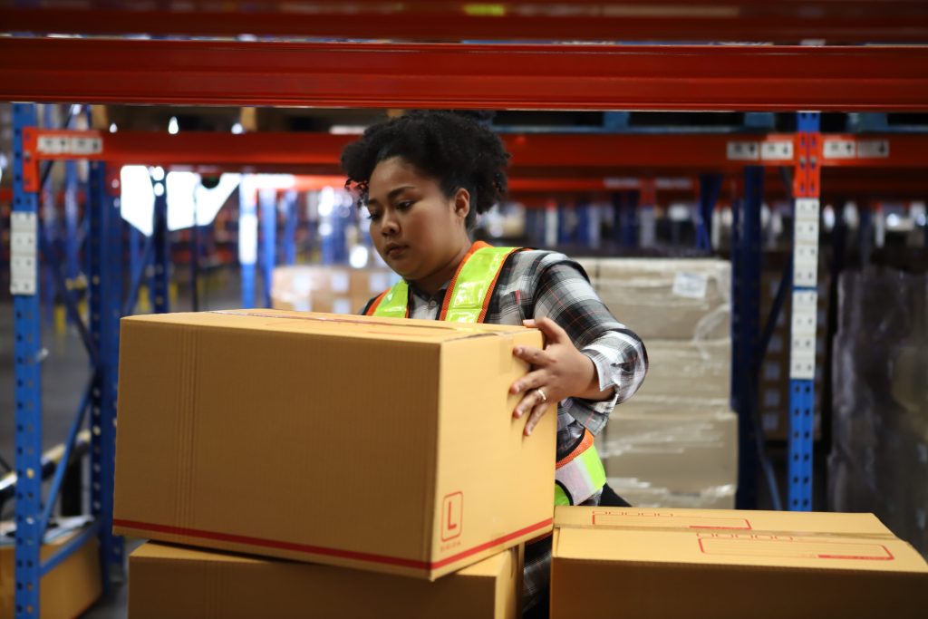 Warehouse worker in a safety vest stacking cardboard boxes in front of blue and red pallet racking