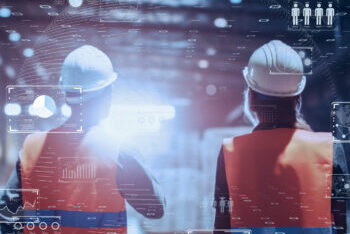 Two workers in hard hats and orange safety vests viewed from behind with digital data overlays