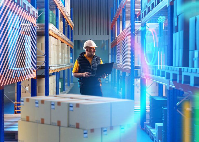 Worker in a hard hat using a laptop among warehouse racks with digital data overlays