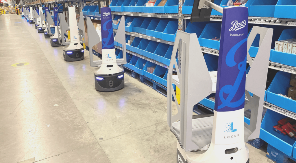 Row of Boots-branded LocusBots lined up beside blue picking bins in a health and beauty warehouse