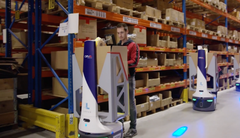 Associate picking items into a CEVA-branded LocusBot in an aisle of orange pallet racking