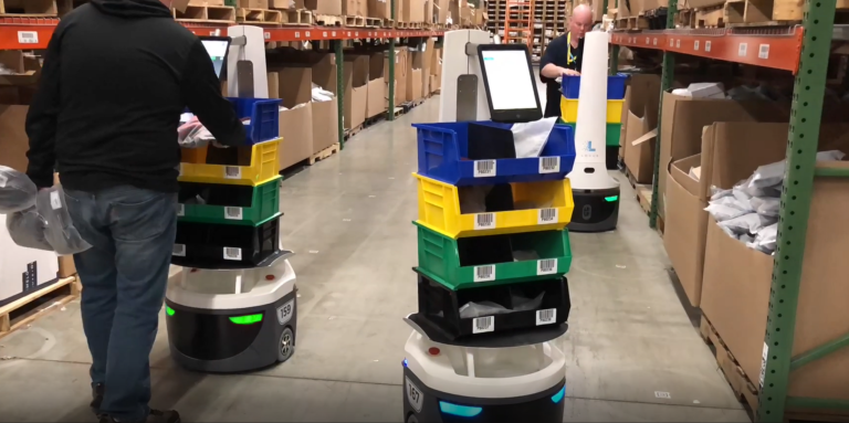Workers picking items into colorful stacked totes carried by LocusBots in a warehouse aisle