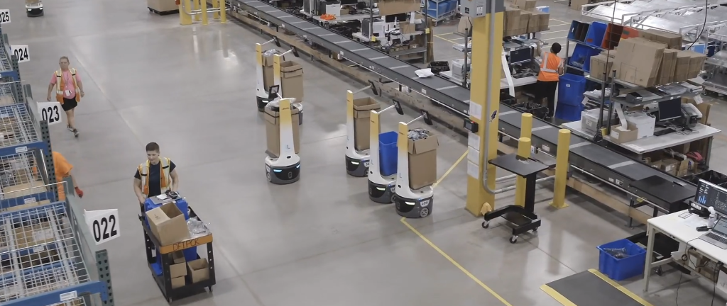 Overhead view of a warehouse with LocusBots carrying totes and boxes near a conveyor as workers push carts