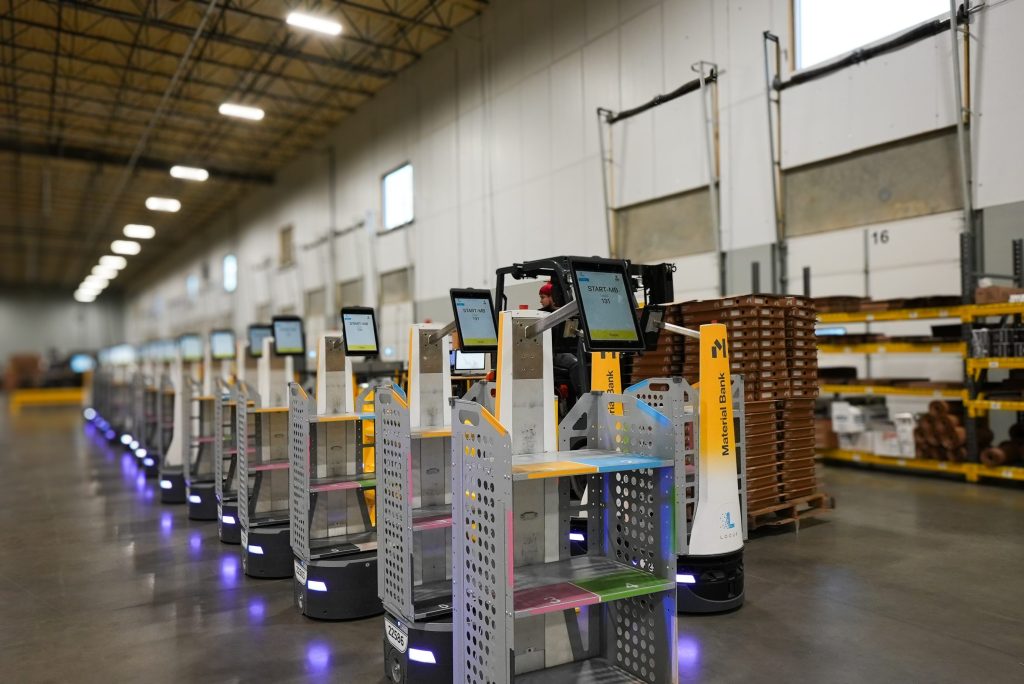 Long line of Material Bank LocusBots with touchscreens and multi-tier shelving carts staged in a warehouse