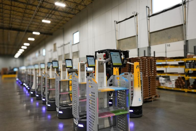 Long line of Material Bank LocusBots with touchscreens and multi-tier shelving carts staged in a warehouse