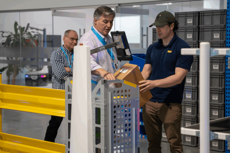 Visitors watching a worker place a parcel on a Locus Robotics robot in a warehouse demo area