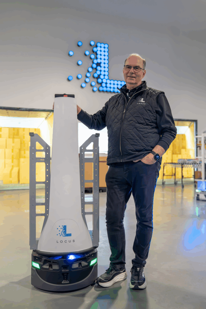 Locus Robotics team member standing beside a LocusBot beneath an illuminated Locus logo wall display
