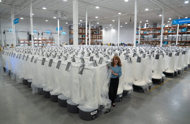 Locus Robotics employee standing among rows of new plastic-wrapped LocusBots filling a large warehouse floor