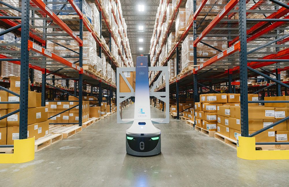 Eversana-branded LocusBot in a warehouse aisle between tall racking stacked with pallets of cardboard cases