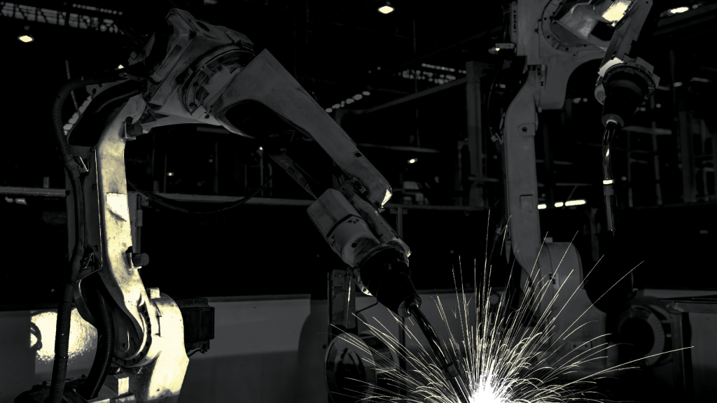 Black and white industrial robotic arms welding on a factory line with bright showers of sparks