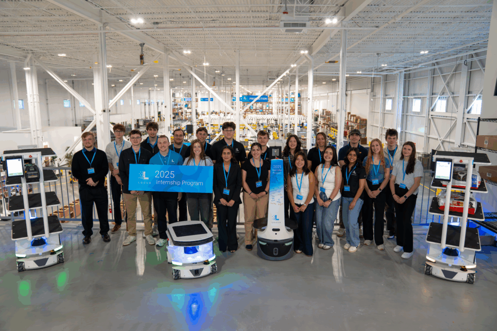 Group of Locus Robotics 2025 interns holding an Internship Program banner with robots in a warehouse