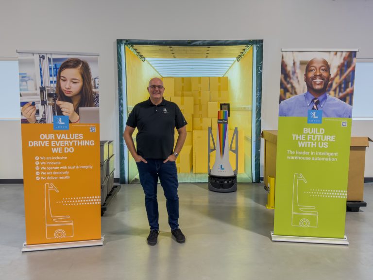 Locus Robotics team member standing between Our Values and Build the Future recruiting banners, a LocusBot behind