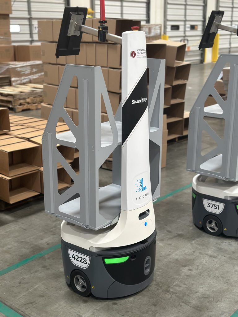 LocusBot co-branded Motivational Fulfillment and Shark Ninja with a gray tote frame, near stacks of flat boxes