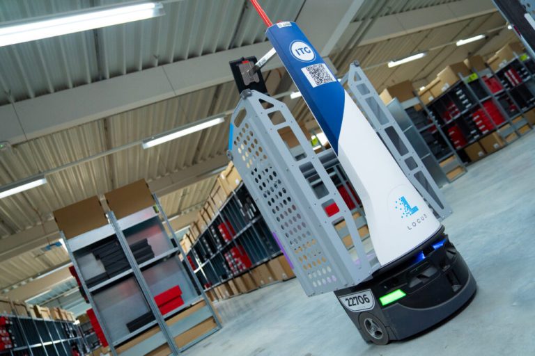 White and blue ITC-branded LocusBot in a warehouse aisle lined with shelves of boxed footwear and apparel