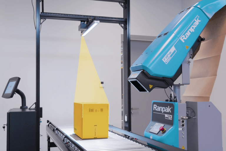 Ranpak packing machine and overhead machine vision scanner over a yellow box on a roller conveyor