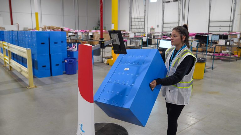 Warehouse associate lifting a large blue tote onto a LocusBot at an induction station