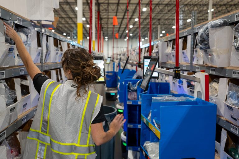 Picker in a safety vest reaching into shelving beside a row of LocusBots with blue carts