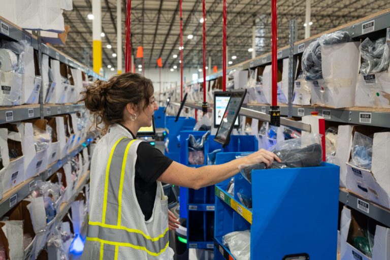 Warehouse associate in a safety vest placing a bagged item into a blue tote on a LocusBot in an aisle