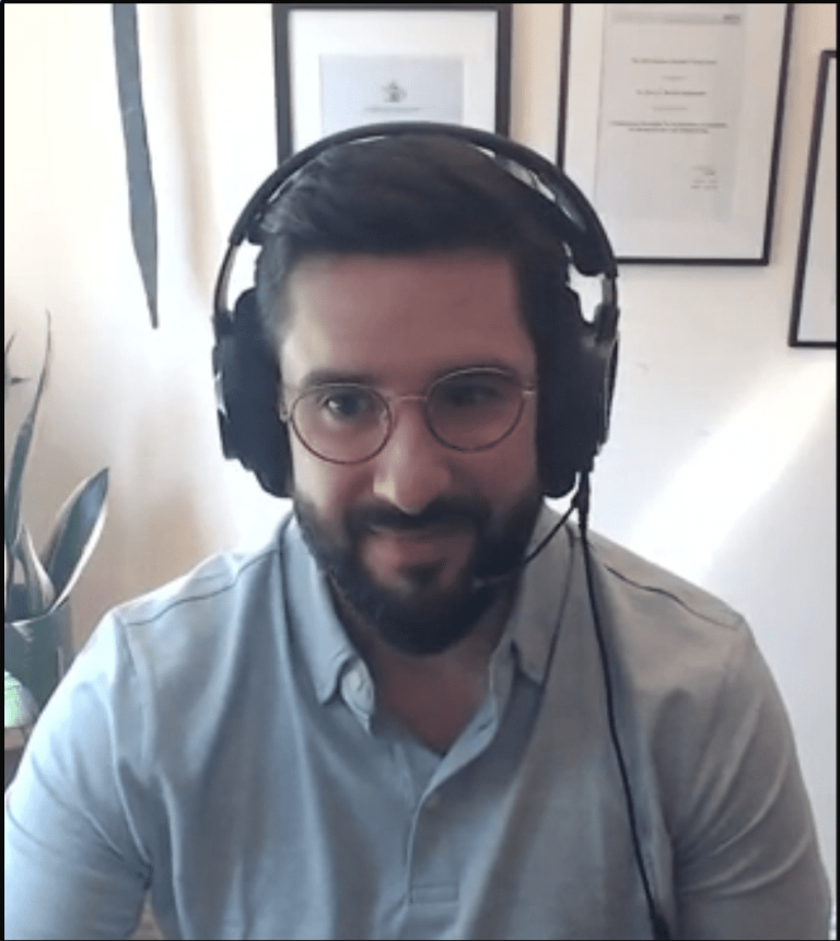 Oscar Mendez wearing a headset and glasses on a video podcast call, framed certificates on the wall behind