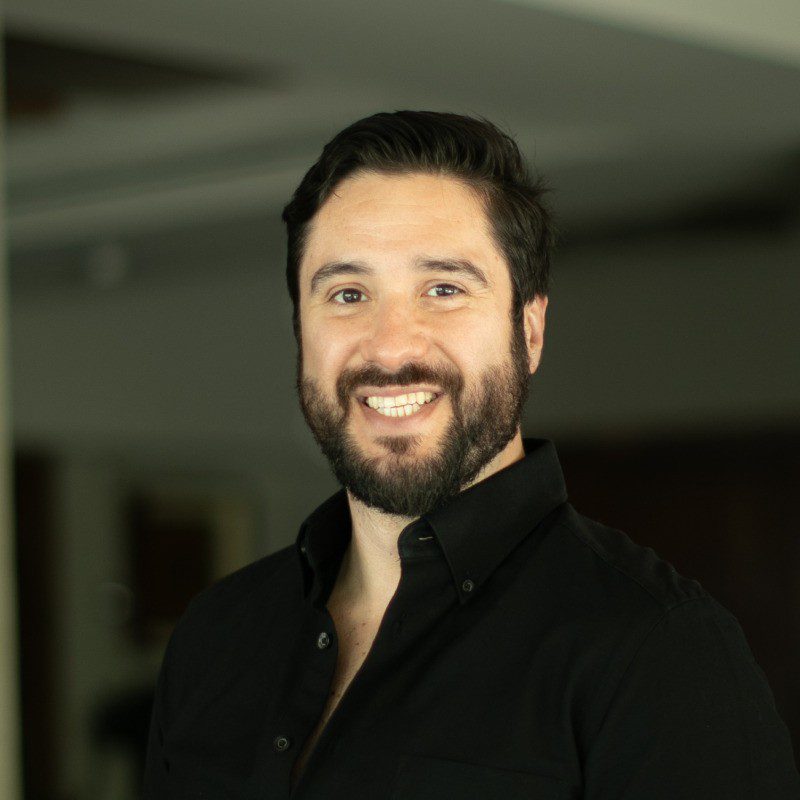 Headshot of Oscar Mendez, smiling with a beard and wearing a black button-up shirt