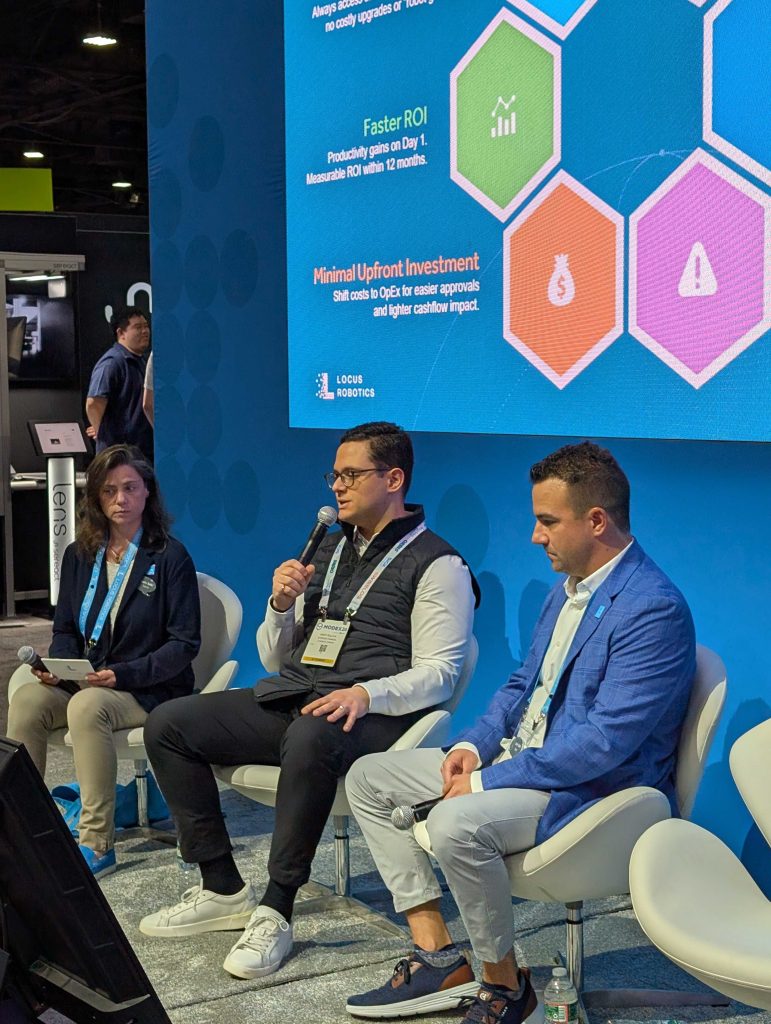 Three panelists in lounge chairs discussing warehouse automation ROI on stage in front of a Locus Robotics slide