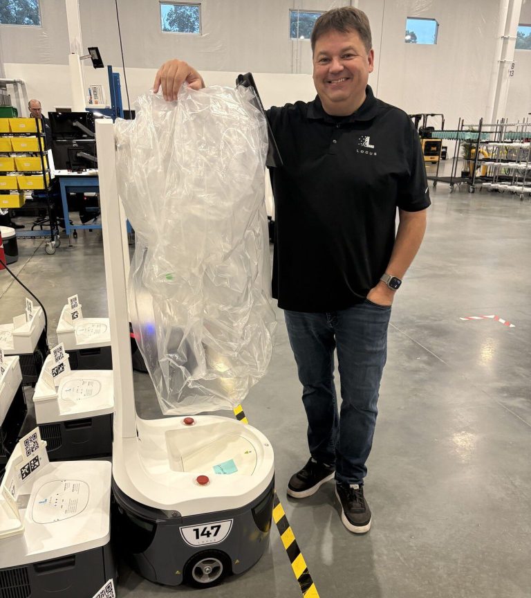 Sean in a Locus polo standing beside a row of LocusBots, one with a bag on its mast