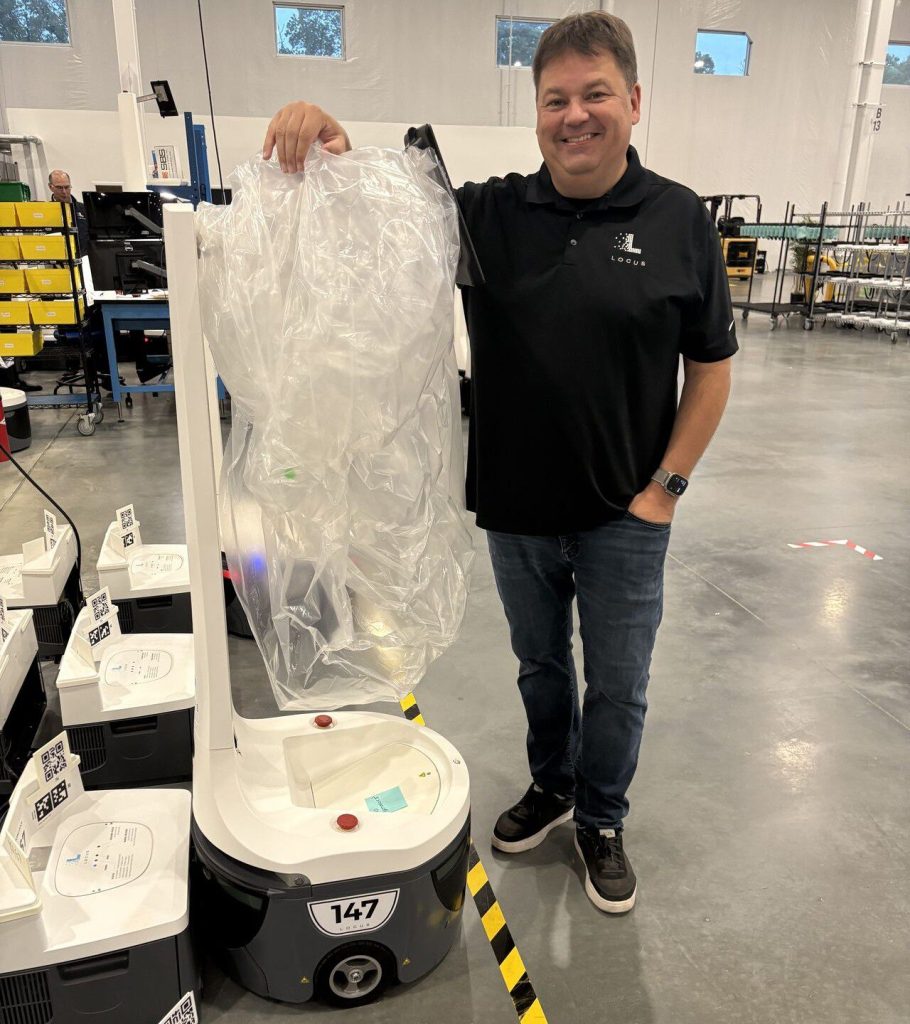 Sean in a Locus polo standing beside a row of LocusBots, one with a bag on its mast