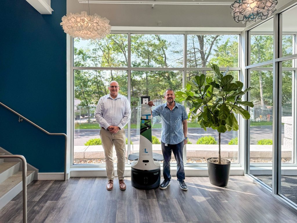 Tracy Simek and Fouad Khalil standing beside a LocusBot in a sunlit office lobby with large windows
