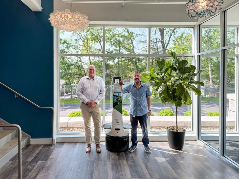 Tracy Simek and Fouad Khalil standing beside a LocusBot in a sunlit office lobby with large windows