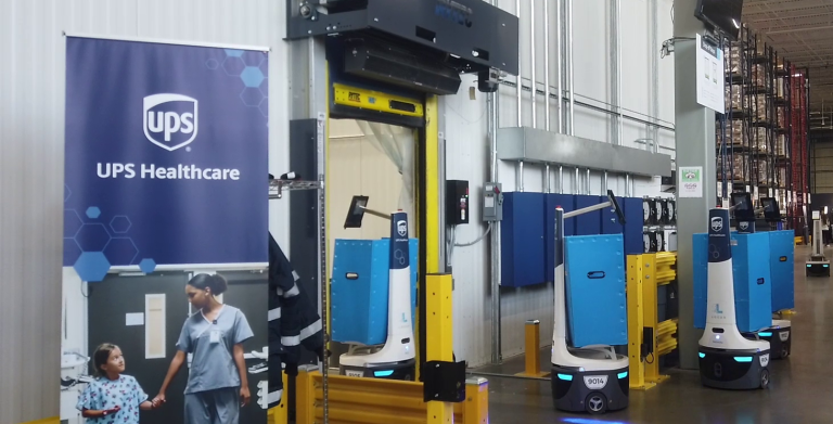 LocusBots with blue totes lined up by a UPS Healthcare banner inside a warehouse