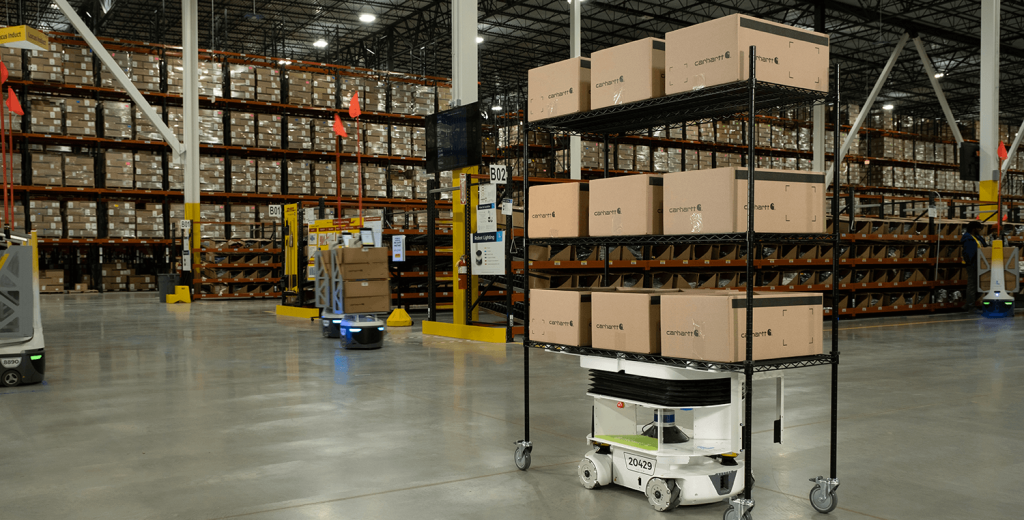 Locus Vector robot carrying a wire cart of boxes across a warehouse with tall pallet racking