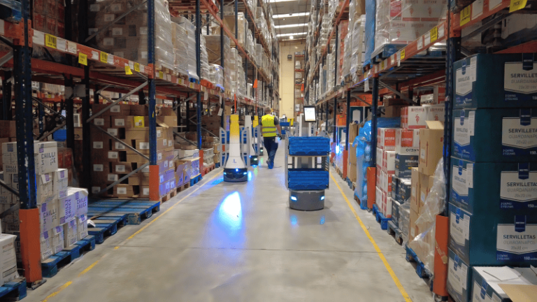 LocusBots and a worker in a high-visibility vest moving down a long aisle of stocked pallet racking