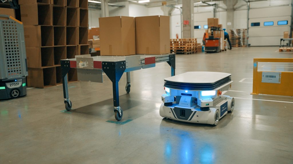 Locus Vector beside a cart loaded with cartons on the Sakalas warehouse floor