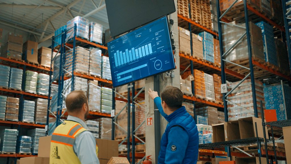 Sakalas team members reviewing a LocusONE performance dashboard mounted in the warehouse
